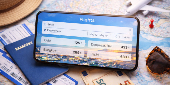 Smartfon z aplikacją do wyszukiwania tanich lotów na tle mapy i akcesoriów podróżnych